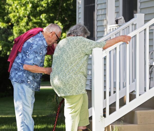 Elderly senior couple arriving home. He is helping her climb slowly up their back porch steps.