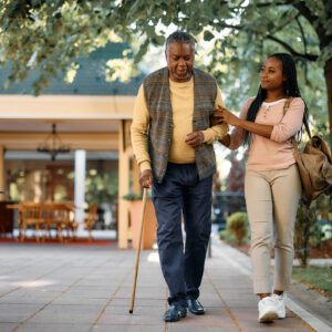 Smiling African American woman walking with her senior father while visiting him at nursing home.